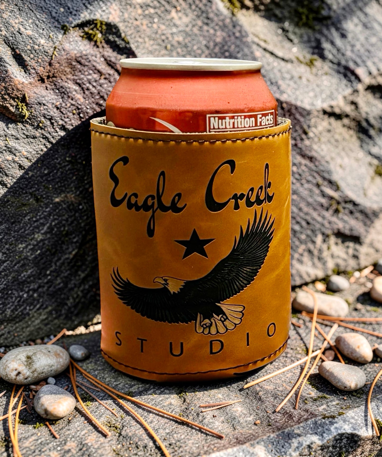 Can cooler with 'Eagle Creek Studio' branding on a rocky surface