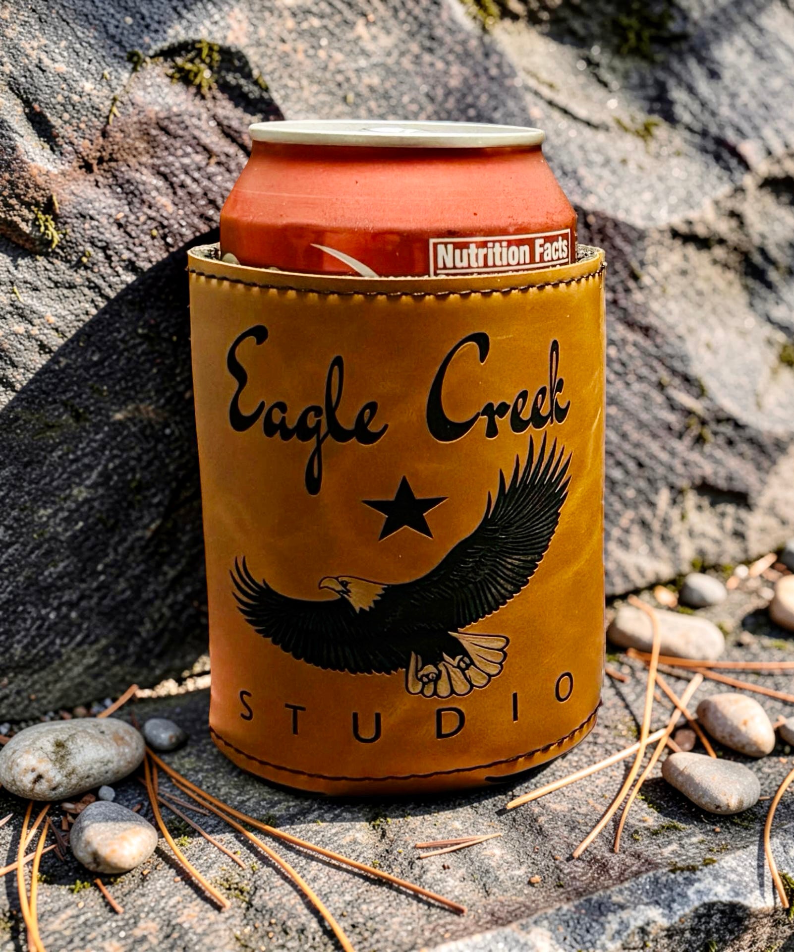 Can cooler with 'Eagle Creek Studio' branding on a rocky surface