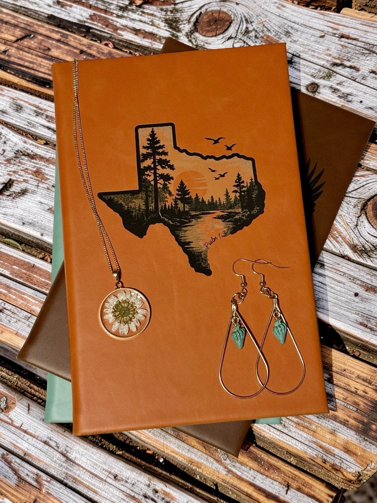 Leatherette notebook with engraved design alongside carefully assembled jewelry, representing everyday gifts & gear from Eagle Creek Studio.